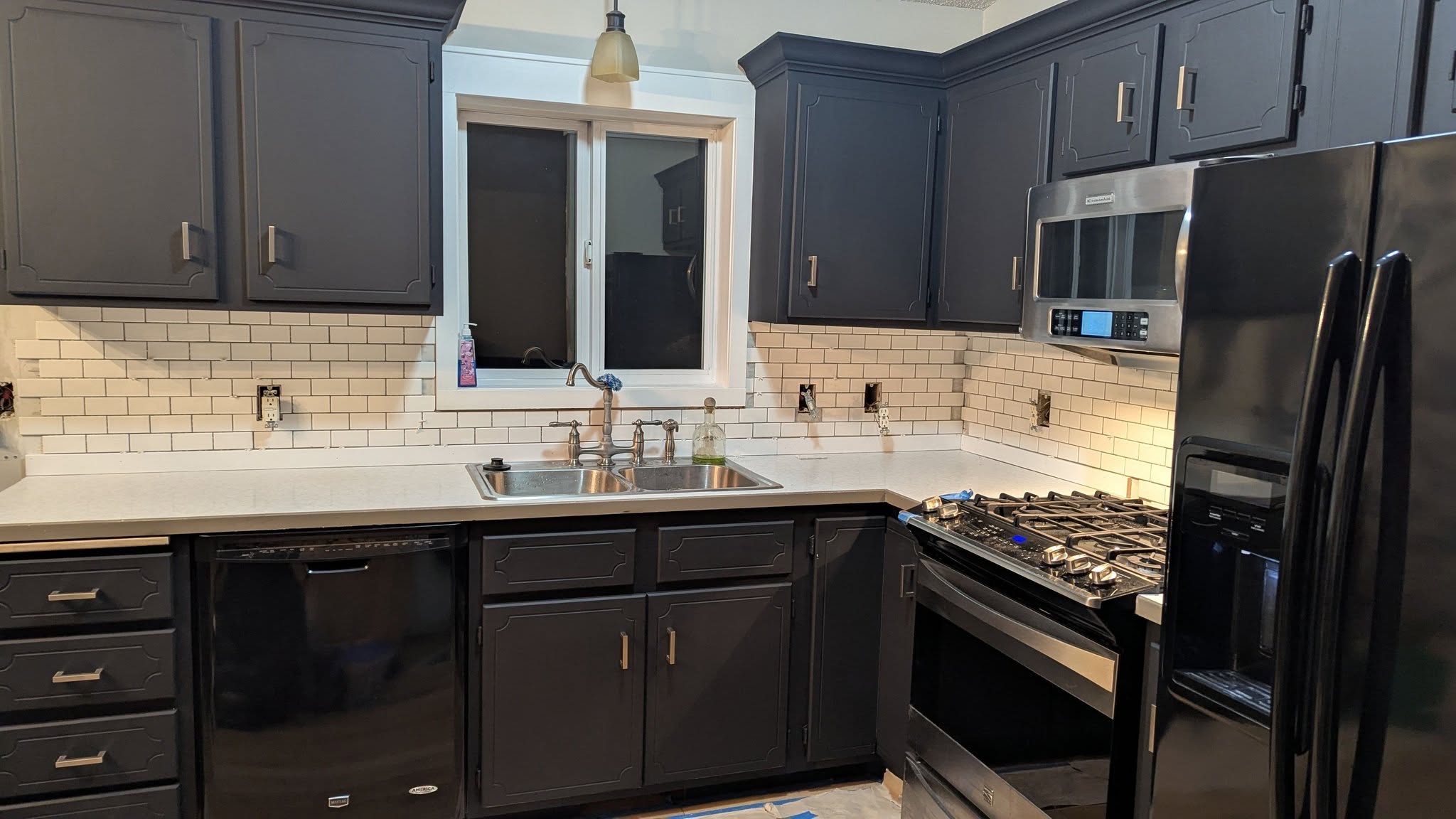 Kitchen cabinets enameled in deep charcoal with brass hardware and a subway tile backsplash