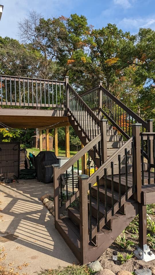 A stained deck staircase with black metal balusters among the trees